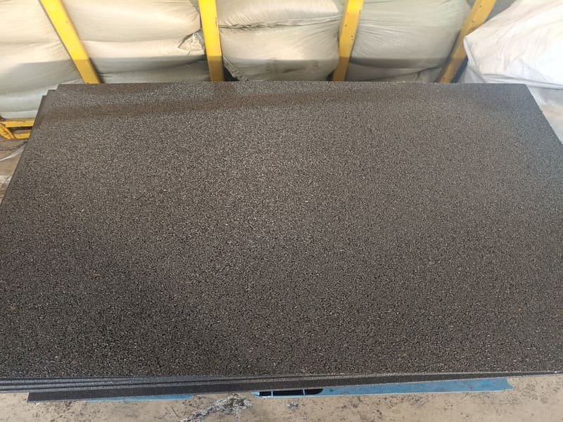 Workers installing black rubber gym flooring rolls in a large commercial fitness center